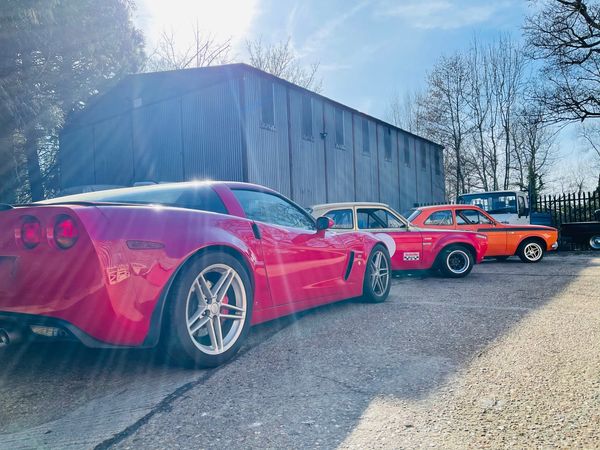 Row of colorful cars parked beside a large shed on a sunny day.