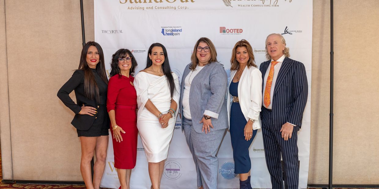 Six professionally dressed people posing in front of a promotional backdrop.
