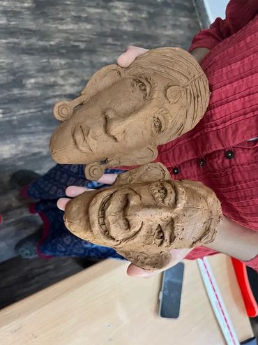 Hands holding two sculpted clay faces with intricate details.