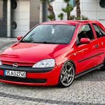 Red Opel hatchback car parked on a cobblestone street.