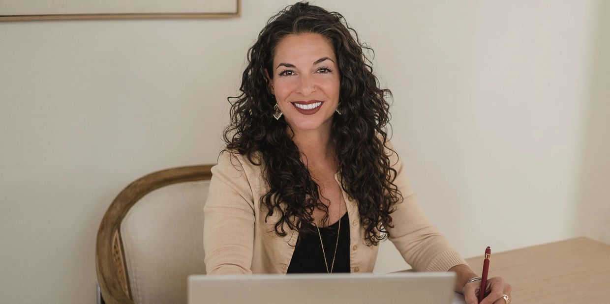 Smiling woman sitting at a desk with a laptop and pen.