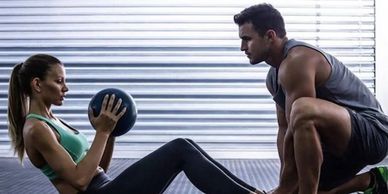 A woman exercises with a medicine ball while a man coaches her.