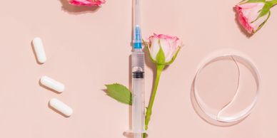 Syringe, capsules, rose, and a transparent condom on a pink background.