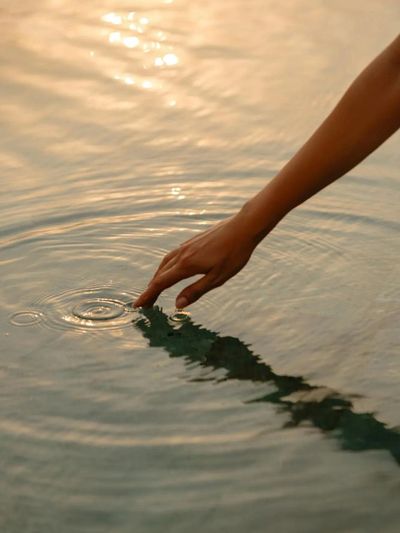 Hand touching calm water creating ripples.