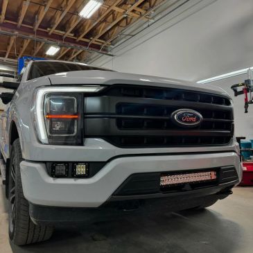 Close-up of a white Ford truck front with custom lights in a garage.
