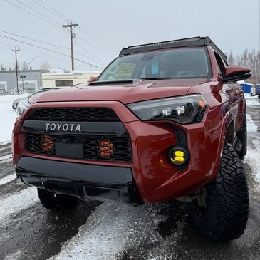 Red Toyota truck with off-road modifications on a snowy street.