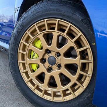 Close-up of a golden alloy wheel on a blue car with neon yellow brake calipers.