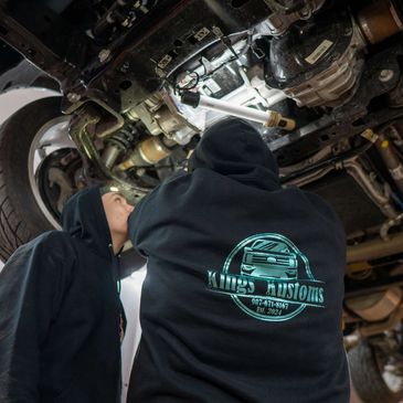 Two mechanics inspecting the underside of a vehicle in a workshop.
