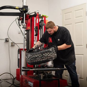 Man mounting a tire on a tire-changing machine indoors.