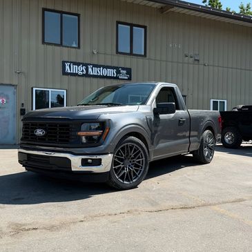 Sleek gray Ford pickup truck parked outside Kings Kustoms shop.
