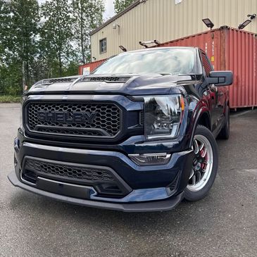 Black Ford Shelby pickup truck parked outdoors near shipping containers.