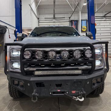 Front view of a rugged truck with multiple lights and a winch in a garage.