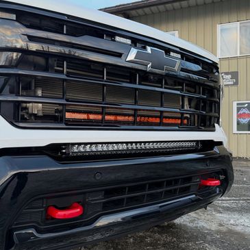 Front grille of a white Chevrolet truck with lights and red tow hooks.