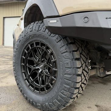 Close-up of a rugged off-road tire on a vehicle with black alloy rims.