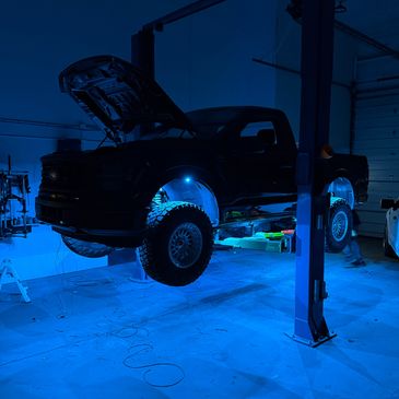 Pickup truck elevated on a car lift in a dimly lit garage with blue lighting.