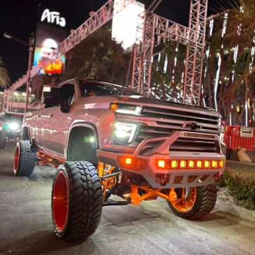 Lifted white truck with orange rims and lights at night in a city.