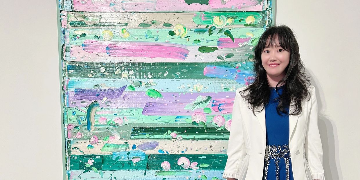Woman in white jacket standing next to colorful abstract painting.