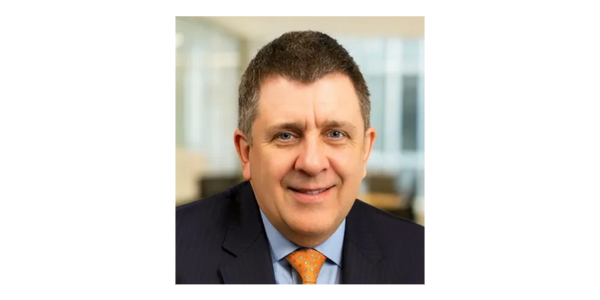 Professional man in suit and orange tie smiling in office setting.