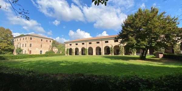 Historic buildings with arches and a lush green lawn under a blue sky.