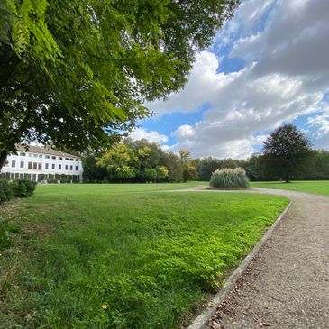 A scenic park with greenery, a pathway, and a building under a partly cloudy sky.