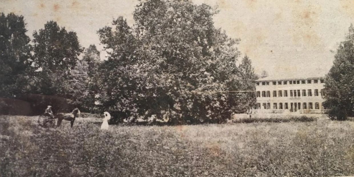 Vintage photo of a person on horseback and a woman in a field near a large building.