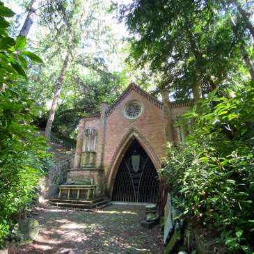 Gothic-style brick building hidden in a lush forest setting.