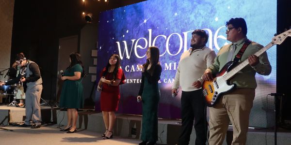Group of musicians and singers performing on stage with a welcome sign in the background.