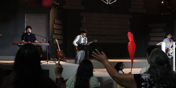 Musicians perform on stage while audience members raise their hands in worship.