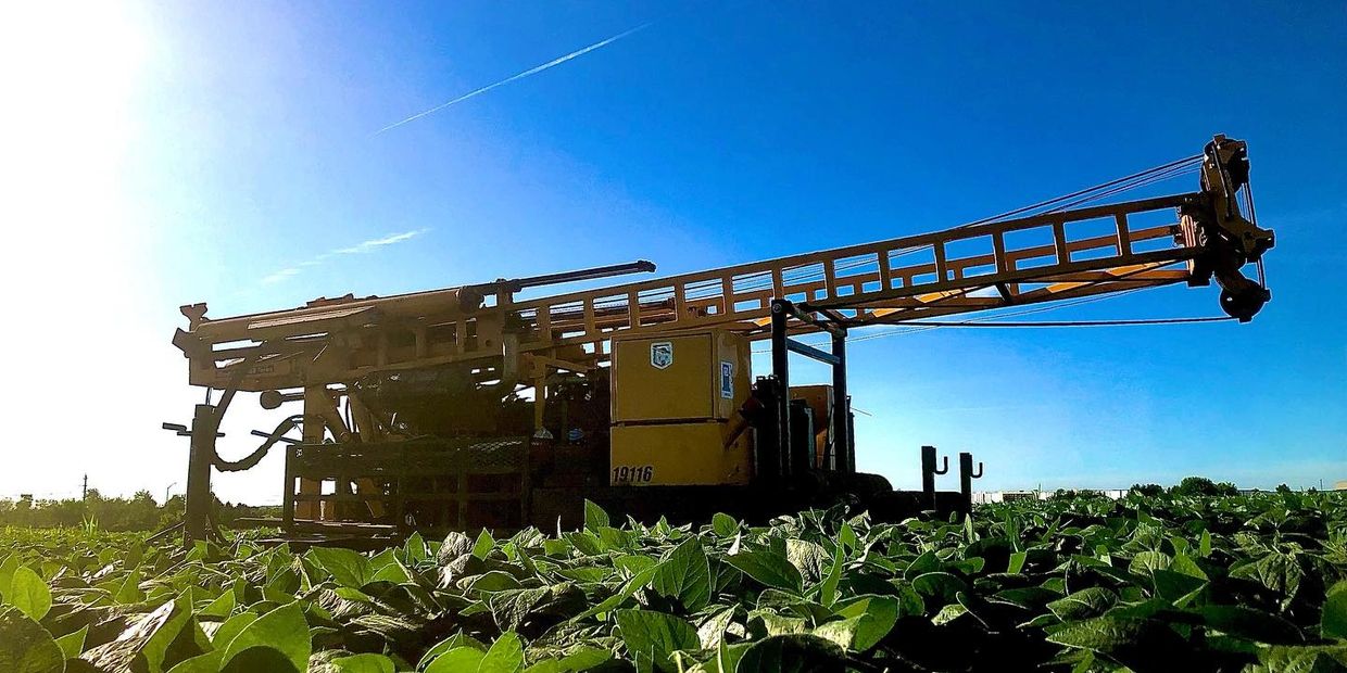 Bright sunny morning on site with drilling equipment deep in a fresh green bean field in the summer.