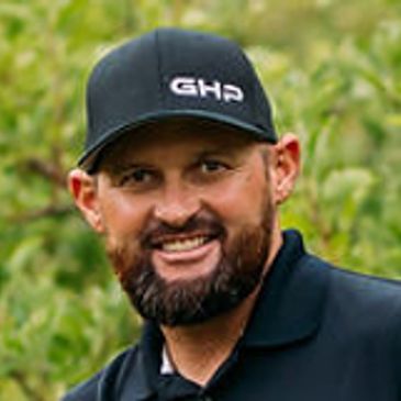 Smiling man with a beard wearing a black GHP cap and black shirt outdoors.