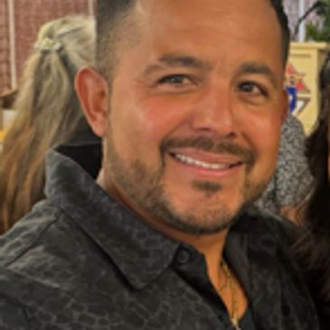 Smiling man with short hair and a beard in a dark shirt.