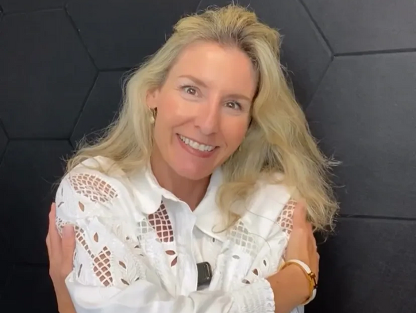 Smiling woman in white blouse with lace details hugging herself.