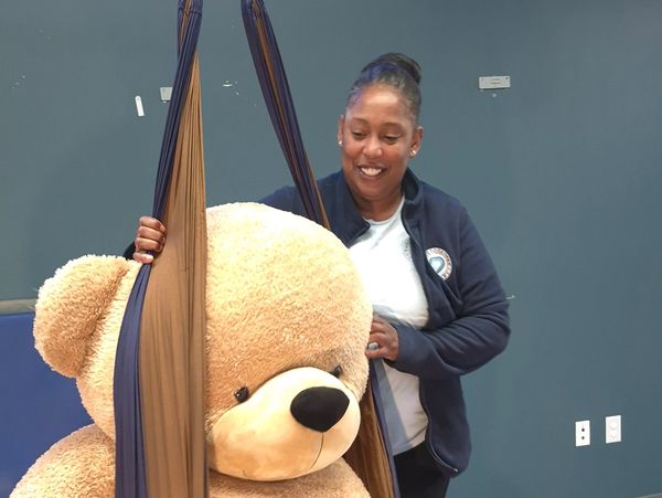 Woman smiling next to a large teddy bear in a fabric sling.