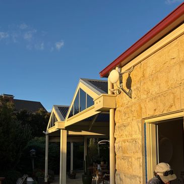 Stone house exterior with sunlit porch roof and clear blue sky.