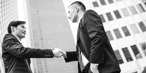 Two businessmen shaking hands outdoors in front of skyscrapers.