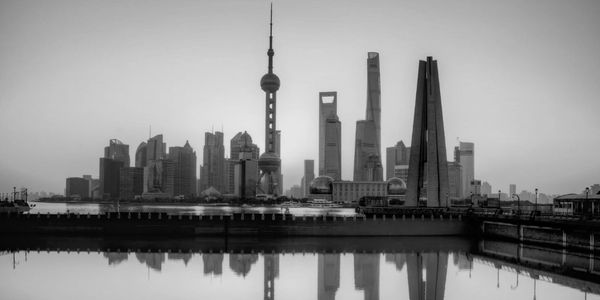 Black and white skyline of Shanghai with reflections in water.