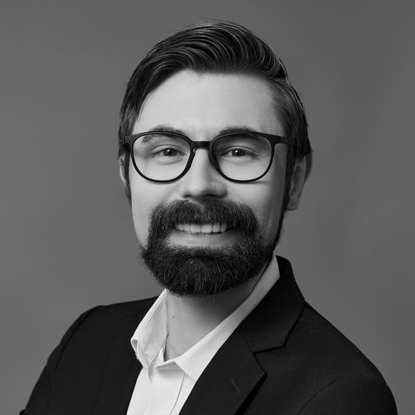 Professional man with beard, glasses, and suit smiling in black and white photo.