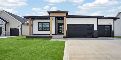 Modern single-story house with black garage doors and well-manicured lawn.