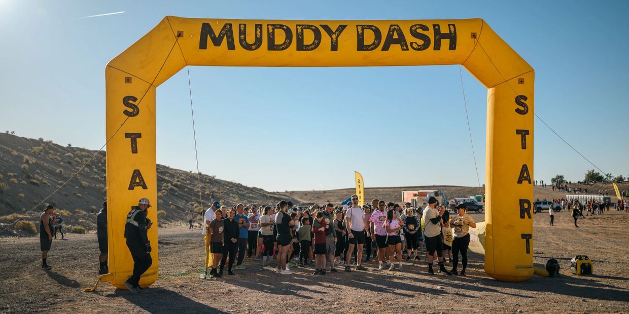 Runners gather at the start of the Muddy Dash race under a yellow inflatable arch.