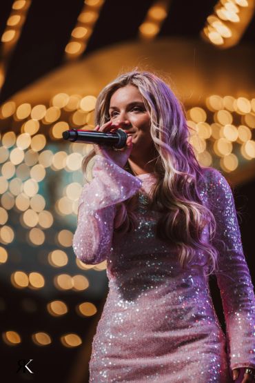 A female singer performing on stage with bright bokeh lights background.