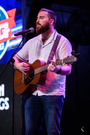 Man with beard playing acoustic guitar and singing on stage.