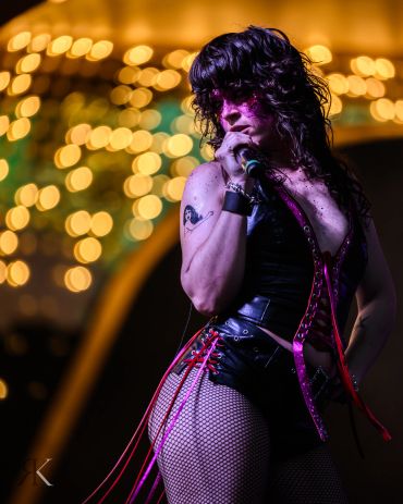 Singer with glitter makeup and fishnet stockings performing on stage with warm bokeh lights behind.