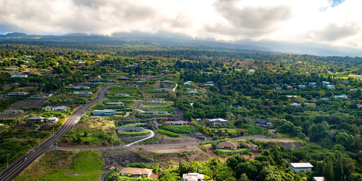 Aerial view of a residential area with greenery and mountains in the background.