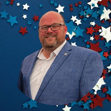 Smiling man in glasses and blue blazer with star-patterned background.