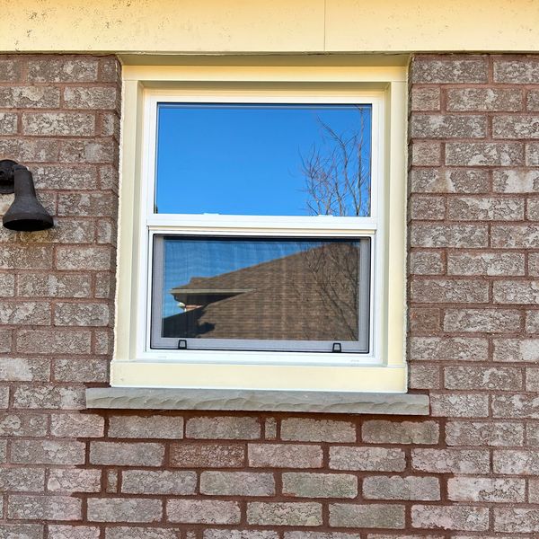 Window on a brick wall with clear sky reflection.