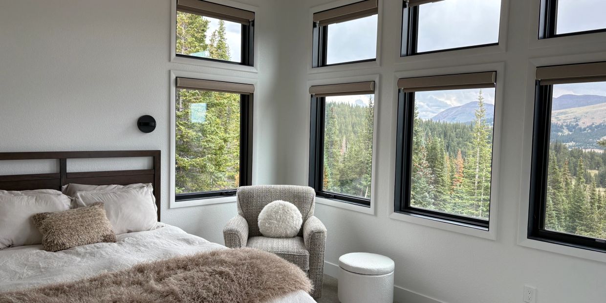 Cozy bedroom with large windows showing forest and mountains.