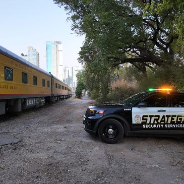 Security vehicle parked near a yellow train in an urban area with trees.