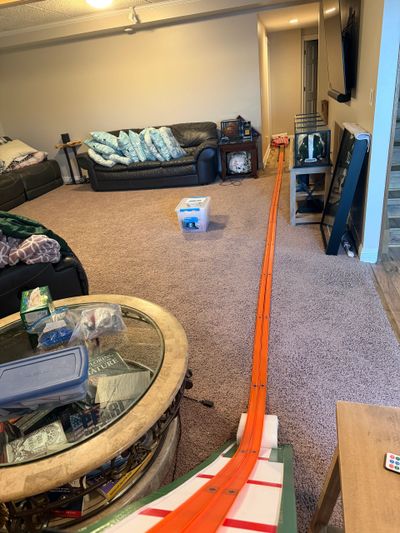 A living room with a long orange toy race track extending from foreground to background.