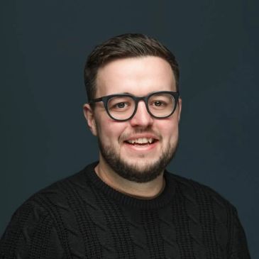 Smiling man wearing glasses and a black sweater.
