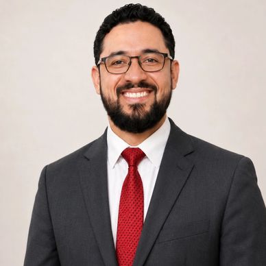 A smiling man in a gray suit and red tie with glasses.
